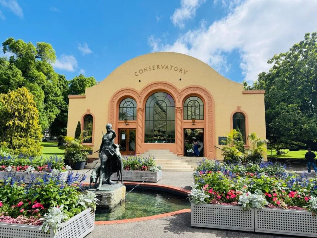 Exterior of Fitzroy Gardens Conservatory with fountain statue and flower beds Melbourne