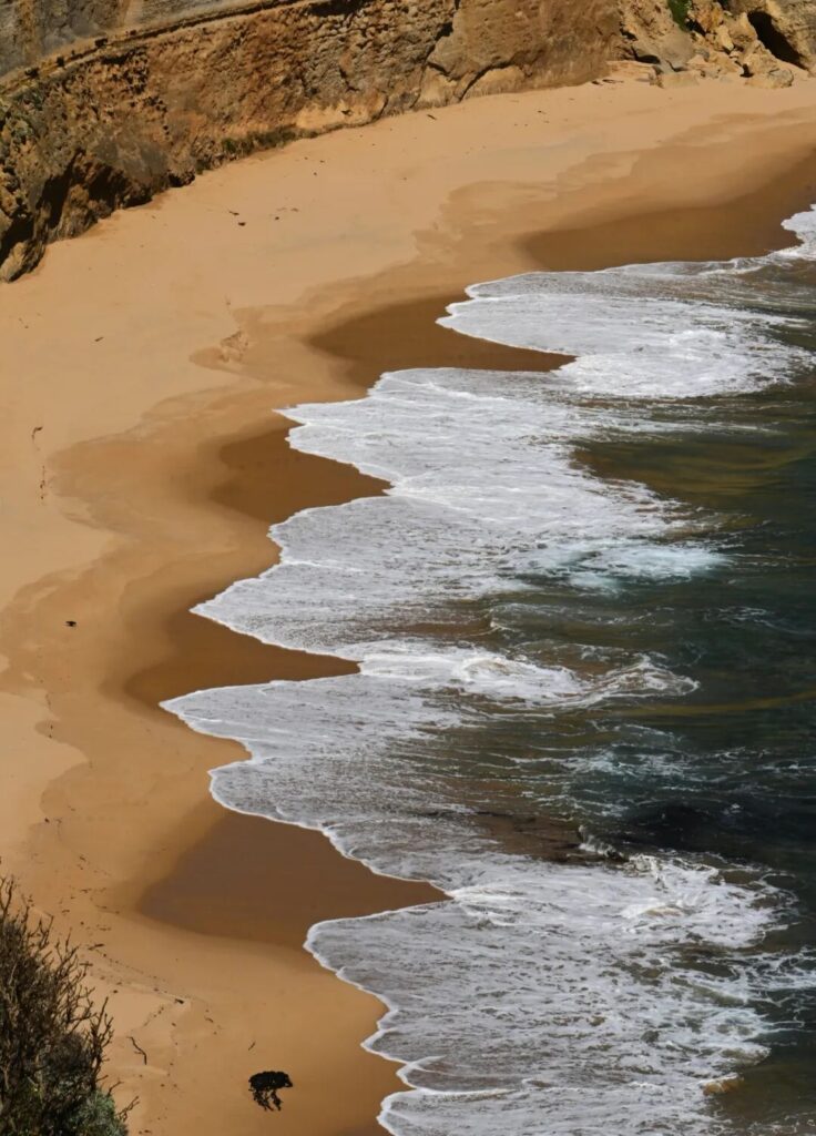 Golden sand and white ocean waves washing ashore at Gibson Steps beach Great Ocean Road