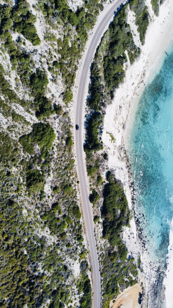 西澳沿海公路航拍，笔直公路旁白色沙滩与碧蓝海水，绿松石色海洋与绿色植被交织