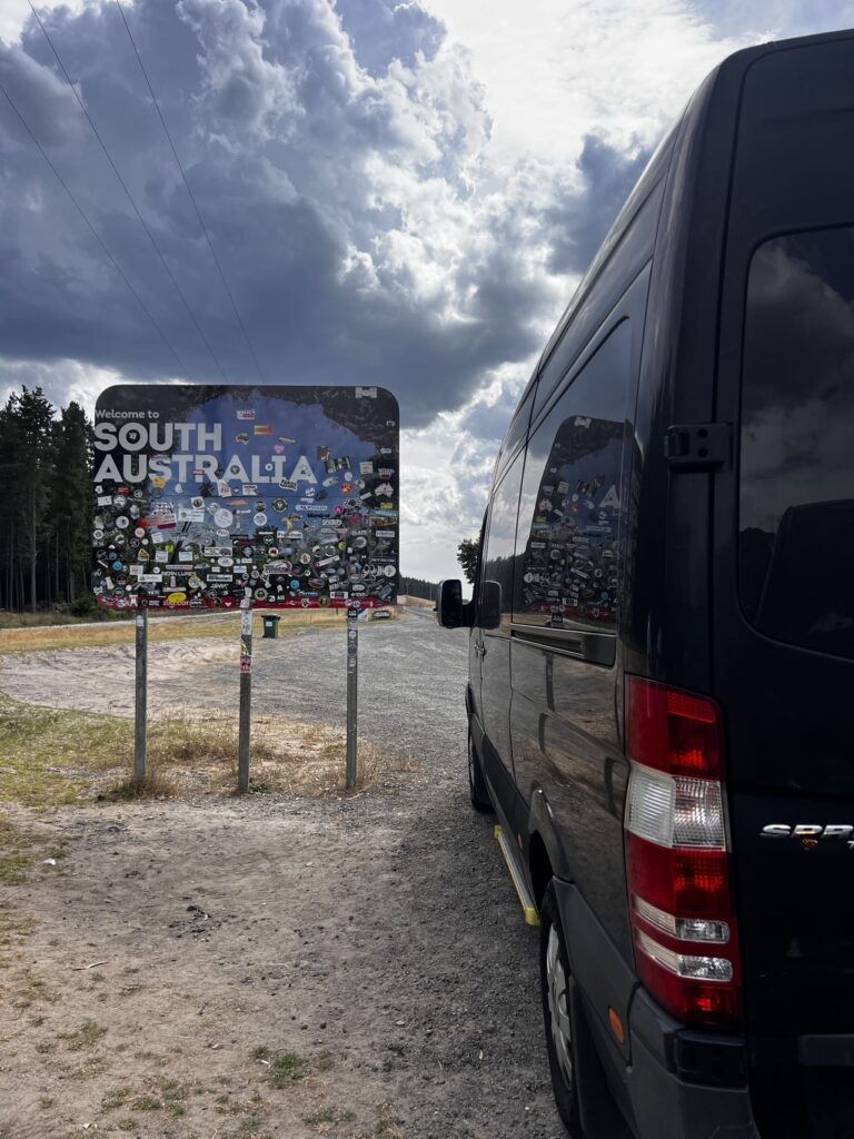 Leo Australia黑色越野房车抵达南澳州界欢迎牌，贴满旅行贴纸的标志性路牌